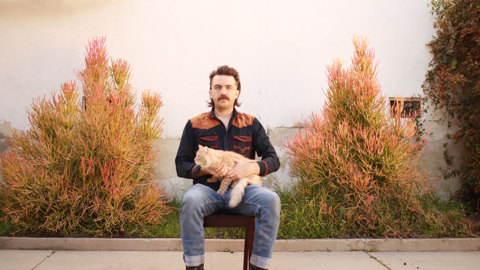 Michael Oberst sitting on a chair outdoors holding an orange cat